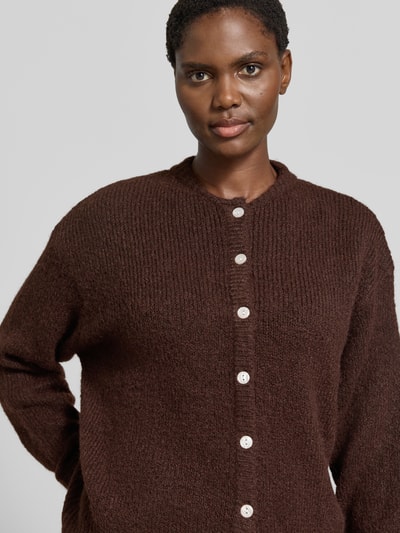 Kobiece model prezentuje kardigan rozpinany z elastycznej mieszanki materiałów z dodatkiem wełny, krój relaxed fit, Model 'Belablue' od ICHI, listwa guzikowa, długie rękawy, okrągły dekolt, obniżone ramiona, prążkowane ściągacze, długość tyłu 57 cm, długość rękawów 71 cm, faktura miękka, kolor brązowy, zbliżenie na górną część tułowia.