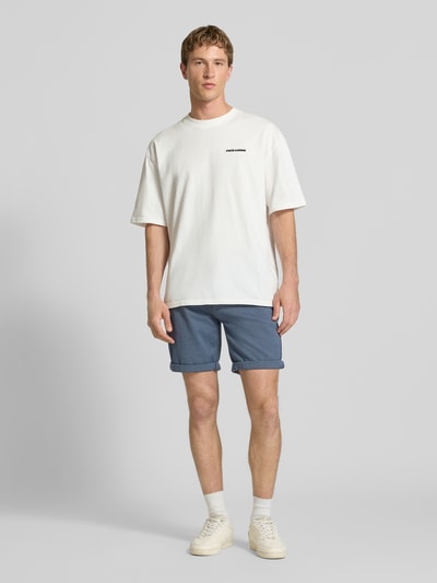 Männermodel trägt Bermudas mit Gürtel und Eingrifftaschen Modell 'NEBRASKA' von Redefined Rebel in Blau, Baumwoll-Mix mit Stretch-Anteil, Ganzkörperansicht von vorne.