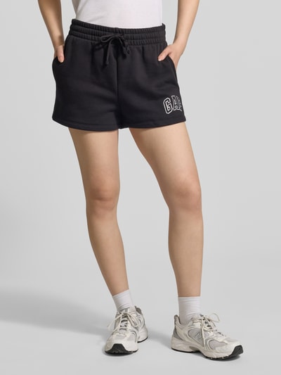 Frauenmodel trägt Sweatshorts mit Logo und elastischem Bund von GAP aus schwarzem Baumwoll-Mix, Regular-Fit, Nahaufnahme Unterkörper, Logo links.