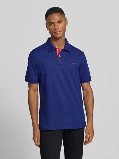 Männermodel trägt Regular Fit Poloshirt mit Logo-Stitching von Gant in Blau, Baumwoll-Mix, Polokragen, Kurzarm, Ganzkörperansicht von vorne.