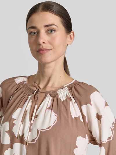 Kobieta nosi Loose Fit Blusenshirt aus reiner Viskose od s.Oliver BLACK LABEL, brązowy z białym kwiatowym nadrukiem, okrągły dekolt z V-wycięciem i wiązaniem, 3/4 rękawy ze ściągaczami, miękka jednolita tekstura, widok z przodu zbliżenie na górną część ciała.