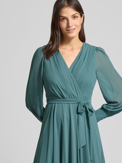 Vrouwenmodel draagt Regular Fit Midikleid mit Taillenband van Christian Berg Cocktail in groen chiffon, V-hals, lange mouwen, tailleband, semi-transparant, blickdichte onderrok, plooien, detailopname bovenlichaam.