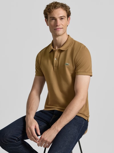 Männermodel trägt Slim Fit Poloshirt aus reiner Baumwolle von Lacoste in hellem Braun, strukturierte Oberfläche, Nahaufnahme Oberkörper.