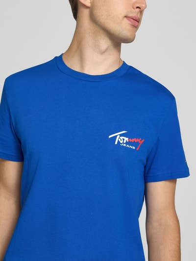 Männermodel trägt Slim Fit T-Shirt aus reiner Baumwolle von Tommy Jeans in kräftigem Blau mit Logo, Nahaufnahme Oberkörper.