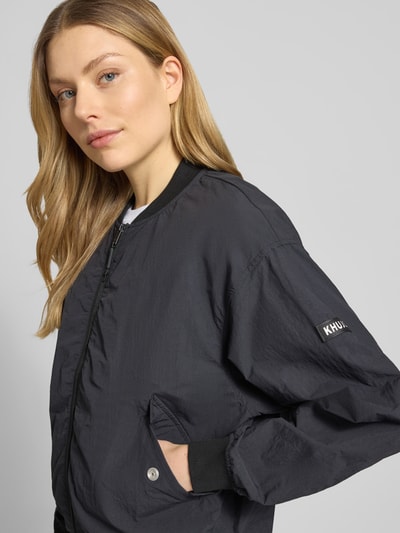 Frauenmodel trägt Jacke mit Pattentaschen Modell 'FACEE' von khujo in Schwarz, Regular-Fit, Stehkragen, Reißverschluss, Umhängetasche, Nahaufnahme Oberkörper. Rückenlänge 60 cm, Schulterbreite 50 cm, Brustweite 55 cm, Ärmellänge 56 cm bei Größe S.
