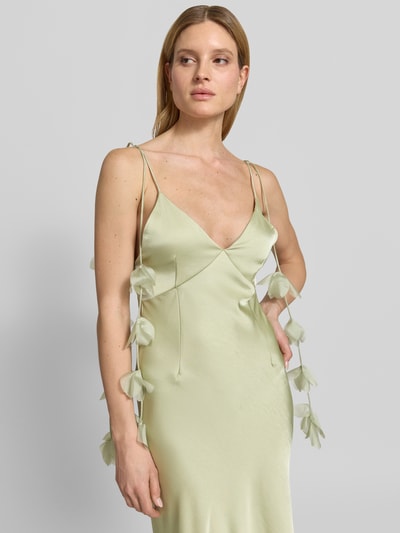 Modelka nosi Abendkleid mit floralen Details Modell 'Colly' od Neo Noir w kolorze jasnozielonym, satynowe, krój slim fit, maksi, głęboki dekolt V, cienkie ramiączka, ozdobne kwiatowe detale na ramiączkach, tekstura gładka, Szerokość w rozmiarze 36: 22 cm, długość tyłu 132 cm, zbliżenie na górną część ciała z przodu.
