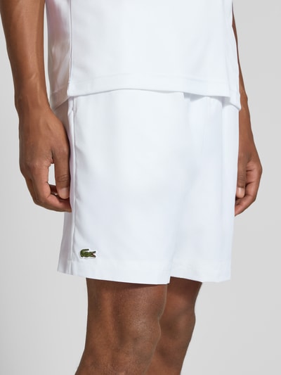 Männermodel trägt Relaxed Fit Shorts mit Logo-Patch von Lacoste in Weiß, glatte Textur, Herren Sportshorts, Nahaufnahme Oberkörper.