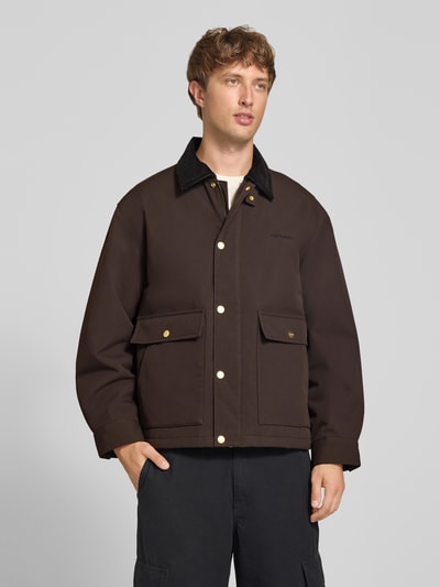Männermodel trägt Relaxed Fit Jacke mit Umlegekragen Modell 'Quentin' von Carhartt Work In Progress in Dunkelbraun mit Cord-Detail, aufgesetzten Taschen und Logo-Stitching, Ganzkörperansicht von vorne.