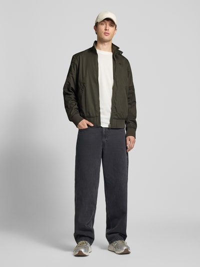 Männermodel trägt Jacke mit Stehkragen und Reißverschluss von G-Star Raw in Olivgrün, kombiniert mit dunkler Hose, Ganzkörperansicht von vorne. Herren Jacke aus Baumwoll-Mix, Regular Fit, bei Größe M mit Rückenlänge 67 cm, Schulterbreite 48 cm, Brustweite 55 cm, Ärmellänge 70 cm.