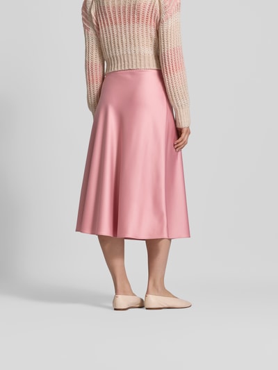 Frauenmodel trägt Midirock aus Satin mit Reißverschluss von Juvia in Rosa, schmale Passform, Midi-Länge, fließende Textur, Ganzkörperansicht Rückansicht.