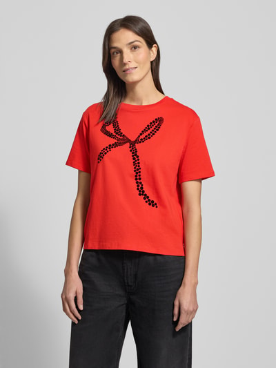 Frauenmodel trägt Oversized T-Shirt aus reiner Baumwolle von Tom Tailor Denim, Optik: Unifarben, Passform: Oversized, Motiv-Print, Rundhals, Kurzarm, Material: reine Baumwolle, leuchtendes Rot mit schwarzer Motiv-Applikation, glatte Struktur, Ganzkörperansicht von vorne.