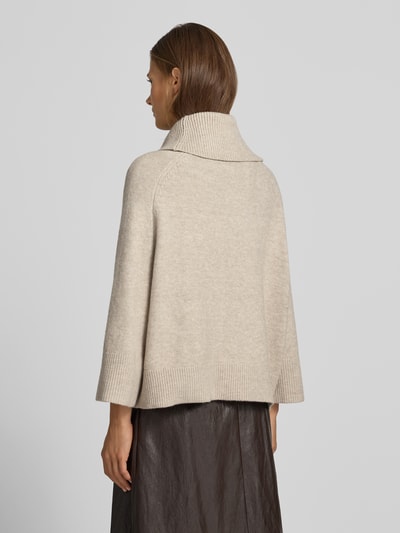 Frauenmodel trägt Rollkragenpullover mit Raglanärmeln von COMMA in Beige, elastischer Material-Mix mit Lanawoll-Anteil, lockerer Schnitt, gerippte Abschlüsse, Rückenlänge 54 cm, Ärmellänge 50 cm, Ganzkörperansicht Rückansicht.