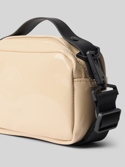 Produktfoto, cremefarbene glatte Handtasche mit Reißverschluss Modell 'BOX BAG MICRO' von RAINS, Label-Detail, verstellbarer schwarzer Schulterriemen, kompakte rechteckige Form, 17x12x8 cm, glänzende Textur