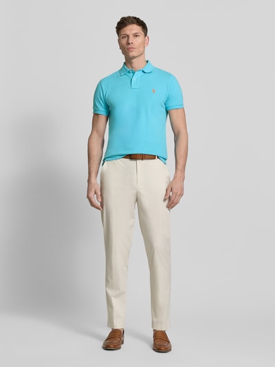 Mannenmodel draagt Regular Fit Poloshirt uit zuivere katoen van Polo Ralph Lauren, effen turquoise, piqué textuur, logo detail, korte mouw, polokraag, V-hals, korte knoopsluiting, asymmetrische zoom met zijsplitten, voorkant volledig zichtbaar, geheellichaamsaanzicht van voren.