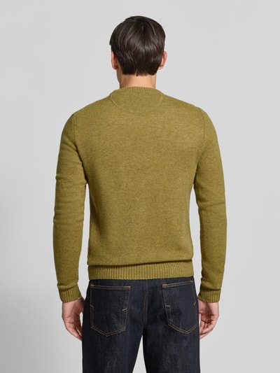 Männermodel trägt Slim Fit Strickpullover aus reiner Wolle mit Label-Stitching von MCNEAL in Olivgrün, gerippte Abschlüsse, Rückenlänge 66 cm, Ärmellänge 69 cm, Ganzkörperansicht Rückansicht.