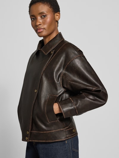 Modelka kobieca ma na sobie Regular Fit Jacke in Leder-Optik mit Umlegekragen od Liu Jo White, kolor ciemnobrązowy, krój regular fit, materiał skóropodobny, wykładany kołnierz, listwa guzikowa, detal z logo, długość tyłu w rozmiarze 36: 60 cm, szerokość ramion w rozmiarze 36: 55 cm, szerokość klatki piersiowej w rozmiarze 36: 60 cm, długość rękawów w rozmiarze 36: 54 cm, prosty krój, wykończenia w brązowych odcieniach, faktura lekko połyskująca, widoczne przeszycia, widok całej sylwetki z przodu.