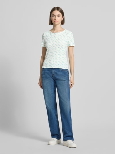 Frauenmodel trägt Slim Fit T-Shirt aus reiner Baumwolle Modell 'TURIEL' von Pieces mit Optik:Allover-Muster, Ripp, Rundhals mit Rüschen, Ärmelform: Kurzarm, Materialverarbeitung: Ripp, Farbe Weiß mit pastellfarbenen Mustern, glatte Textur, Ganzkörperansicht von vorne.