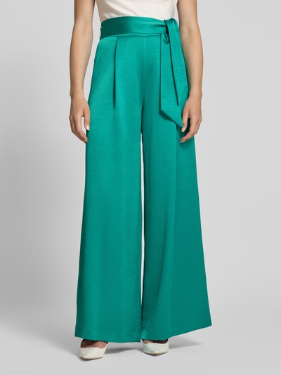 Frauenmodel trägt Relaxed Fit Anzughose aus Satin von Marc Cain, smaragdgrün, Crinkle-Optik, breiter Stoffgürtel, Ganzkörperansicht von vorne.