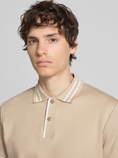 Männermodel trägt Slim Fit Poloshirt mit Strukturmuster Modell 'FABLE' von Blend in Beige, Knopfleiste, Nahaufnahme Oberkörper.