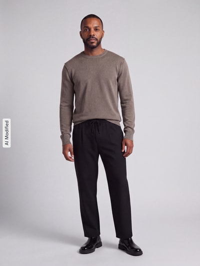 Männermodel trägt Regular Fit Pullover aus reiner Baumwolle von ONLY & SONS in Beige mit schwarzer Hose, Ganzkörperansicht von vorne, KI-modifiziertes Bild.
