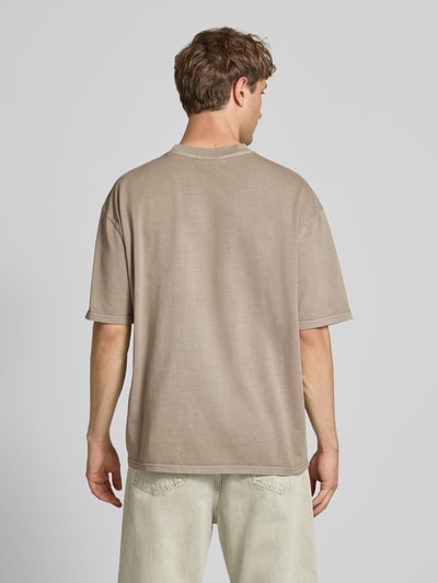 Männermodel trägt Oversized T-Shirt mit Label-Stitching von Pegador in Beige, aus Baumwoll-Mix, Rundhalsausschnitt, Rückenlänge 70 cm, Ganzkörperansicht Rückansicht.