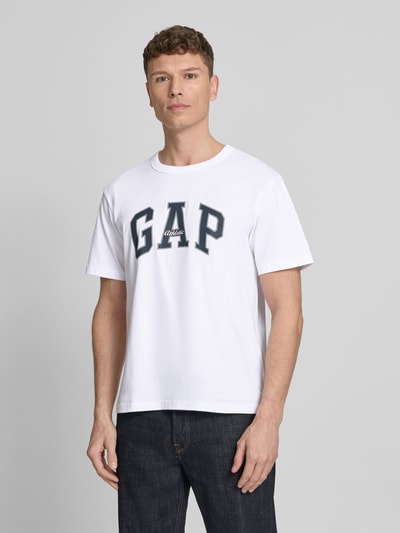 Männermodel trägt T-Shirt mit Logo und Rundhalsausschnitt von GAP in Weiß aus Reiner Baumwolle, Regular-Fit, Logo, Ganzkörperansicht von vorne. Rückenlänge bei Größe M: 66 cm.