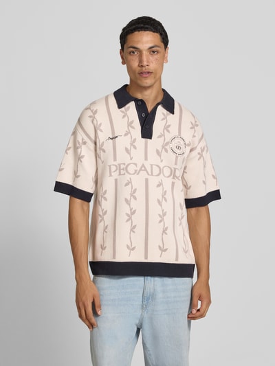 Männermodel trägt Relaxed-Fit Poloshirt mit Logo-Stitchings Modell 'Kinsale' von Pegador aus Reine Baumwolle in Creme mit Kontrastkante, Gerippter Polokragen und Knopfleiste, Rückenlänge bei Größe M 69 cm, Ganzkörperansicht von vorne.