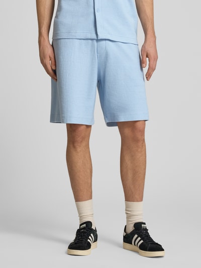 Męski model trägt szorty z wyhaftowanym logo Shorts mit Label-Stitching von REVIEW, mieszanka bawełny, krój regular fit, fakturowany wzór, szerokość w rozmiarze M: 42 cm, długość wewnętrzna nogawki w rozmiarze M: 22 cm, jasnoniebieski, całkowity widok z przodu