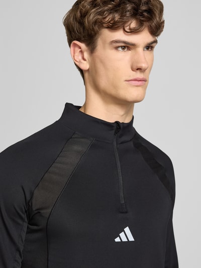 Männermodel trägt Sweatshirt mit Stehkragen von adidas Training in Schwarz, Material-Mix mit Stretch, Label-Print, Nahaufnahme Oberkörper.