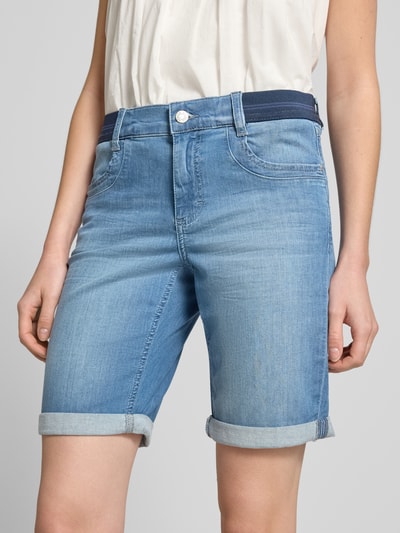 Kobiece modelka nosi Jeansshorts mit Umschlag und elastischem Bund od Angels z mieszanki bawełny i elastanu, krój regular fit, kolor jasnoniebieski, szerokość w rozmiarze 36: 39 cm, długość wewnętrzna nogawki w rozmiarze 36: 30 cm, tekstura gładka, widoczne wywinięcie na nogawkach, zbliżenie na dolną część ciała, widok z przodu