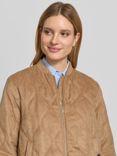 Vrouwenmodel draagt Jacke mit Stehkragen und Zweiwege-Reißverschluss van Fuchs Schmitt in lichtbruin met doorgestikte naden, regular fit, opstaande kraag, tweewegritssluiting, ruglengte maat 36: 57 cm, schouderbreedte maat 36: 47 cm, borstwijdte maat 36: 43 cm, mouwlengte maat 36: 67 cm. Nahaufnahme bovenlichaam.