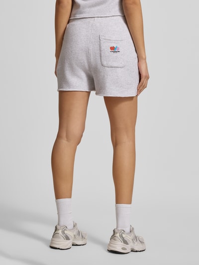 Männermodel trägt Sweatshorts mit elastischem Bund Modell 'TUBAY' von American Vintage, jasnoszary kolor, bawełna z elastanem, prosta forma, tylna kieszeń, kieszenie boczne, widok całej sylwetki z tyłu.