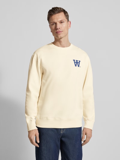 Männermodel trägt Sweatshirt mit Logo-Print Modell 'NOEL' von Wood Wood aus reiner Baumwolle in Creme, lockere Passform, Ganzkörperansicht von vorne.