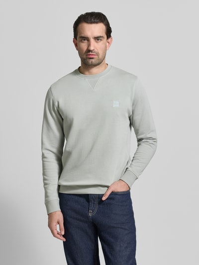 Männermodel trägt Relaxed Fit Sweatshirt aus reiner Baumwolle Modell 'WESTART' von BOSS Orange in Hellgrau, unifarben, Label Patch, Rundhals, Langarm, Sweatstoff, Ganzkörperansicht von vorne.