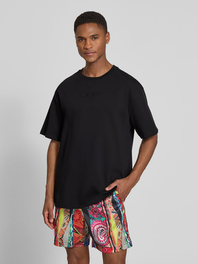 Männermodel trägt schwarzes Relaxed Fit T-Shirt mit Logo-Stitching Modell 'Ikarus' von COLUCCI aus reiner Baumwolle; Ganzkörperansicht von vorne