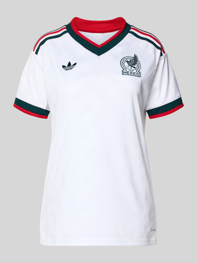 Modelka nosi Mexiko Auswärtstrikot 2026 od adidas Sportswear, biały, kolorowe pasy, krój regular fit, wzór strukturalny, logo, V-dekolt, krótki rękaw; widok na cały przód.