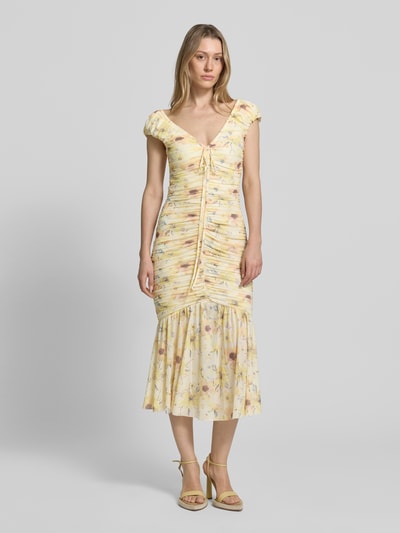 Frauenmodel trägt Midikleid mit Drapierungen und V-Ausschnitt von Little Mistress, Material-Mix mit Stretch-Anteil, figurbetonter Schnitt, Rückenlänge bei Größe 36: 120 cm, florales Muster in Gelb und Pastell, Ganzkörperansicht von vorne.