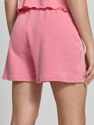 Frauenmodel trägt Regular Fit Shorts aus Baumwoll-Mix Modell 'MISTY' von Only, Optik: Allover-Muster, gestreift, Materialverarbeitung: Seersucker, Bundabschluss: elastisch, Farbmix aus Pink und Weiß, Nahaufnahme Rückansicht.