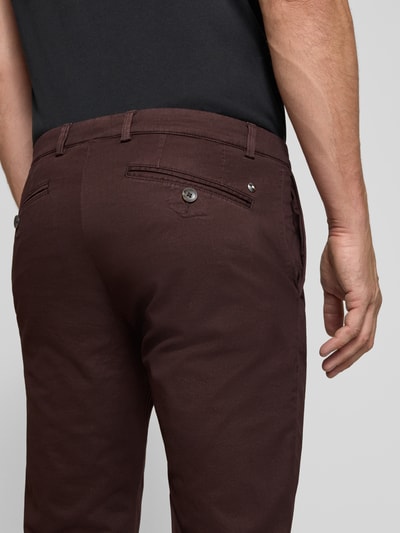 Männermodel trägt Slim Fit Chino aus Baumwoll-Mix von bugatti in Dunkelbraun, Gesäßtaschen, Nahaufnahme Rückansicht.