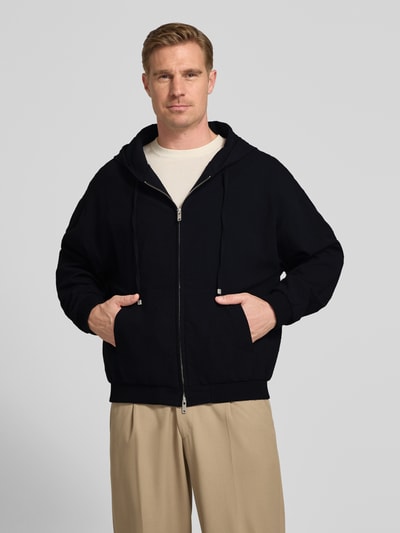 Männermodel trägt Relaxed Fit Sweatjacke aus reiner Baumwolle Modell 'Hootailored262X' von HUGO, schwarze Unifarben-Optik, Reißverschluss, Label-Detail, Sweatkapuze mit Tunnelzug, aufgesetzte Seitentasche, gerippter Ärmelabschluss und Rumpfabschluss, Sweat-Material, Ganzkörperansicht von vorne.