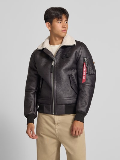 Männermodel trägt Bomberjacke mit Label-Patch und Kentkragen von Alpha Industries in Schwarz mit Teddyfellkragen, Reißverschluss, Nahaufnahme Oberkörper.