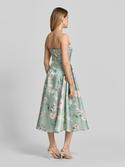 Männermodel trägt Cocktailkleid im Off-Shoulder-Look von Swing w zielone kwiaty, krój taliowany, sukienka midi, zamek błyskawiczny z tyłu, długość tyłu 98 cm, szerokość w rozmiarze 36: 41 cm, widok całej sylwetki z tyłu