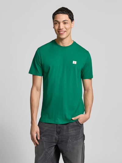 Männermodel trägt T-Shirt mit Label-Badge von Calvin Klein Jeans in Grün, reine Baumwolle, Regular Fit, Rundhals, Ganzkörperansicht von vorne.