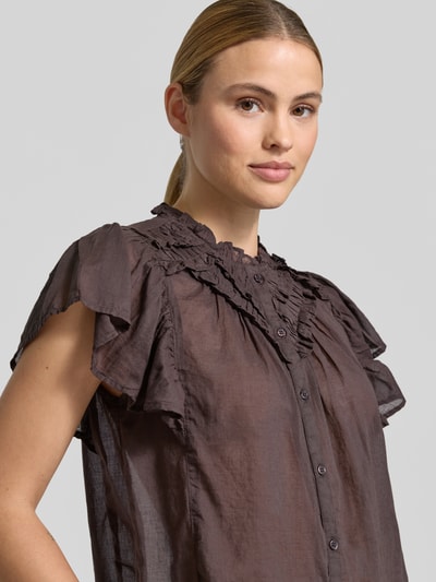 Frauenmodel trägt Regular Fit Bluse mit Rüschenbesatz Modell 'Vinsa' von Neo Noir in dunklem Braun, Reine Baumwolle, Kurzärmelig, Stehkragen, durchgängige Knopfleiste, Nahaufnahme Oberkörper.