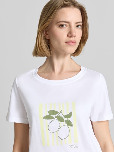 Frauenmodel trägt Regular Fit T-Shirt aus reiner Baumwolle von s.Oliver RED LABEL mit Motiv-Print, Pailletten und Label-Applikation in Unifarben, weiß-gelbe Farben, Jerseystruktur, Rundhals, kurzarm, Nahaufnahme Oberkörper.