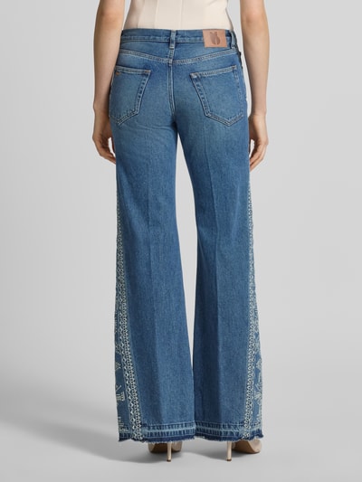 Frauenmodel trägt Flared Jeans mit Motiv-Stitching Modell 'VIVY' von Bash, Reine Baumwolle, ausgestellter Schnitt, 5-Pocket-Design, Knopf-Reißverschluss, mittleres Blau, sichtbare dekorative Nähte, Bundweite 38 cm, Innenbeinlänge 87 cm, Ganzkörperansicht Rückansicht.