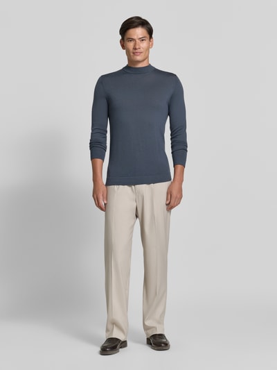 Männermodel trägt Slim Fit Longsleeve aus reiner Schurwolle Modell 'Arwon' von DRYKORN in Blau, kombiniert mit heller Hose, Stehkragen, reine Schurwolle, Ganzkörperansicht von vorne.
