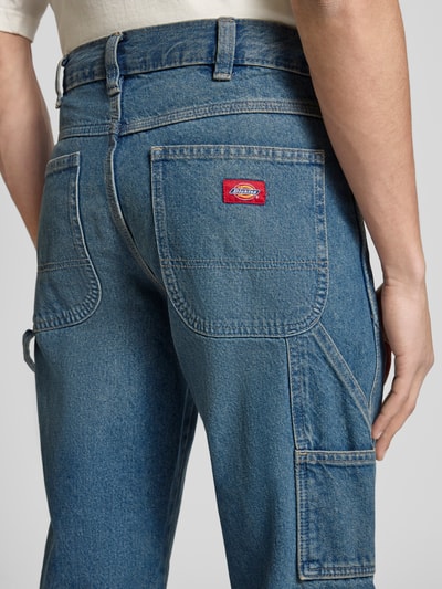 Mężczyznamodel nosi Regular Tapered Fit Jeans im Used-Look od Dickies z bawełny, niebieski denim, kieszenie, detal z tyłu, zbliżenie na biodra. Szerokość w rozmiarze 32/32: 40 cm, długość nogawki wewnętrznej: 80 cm.