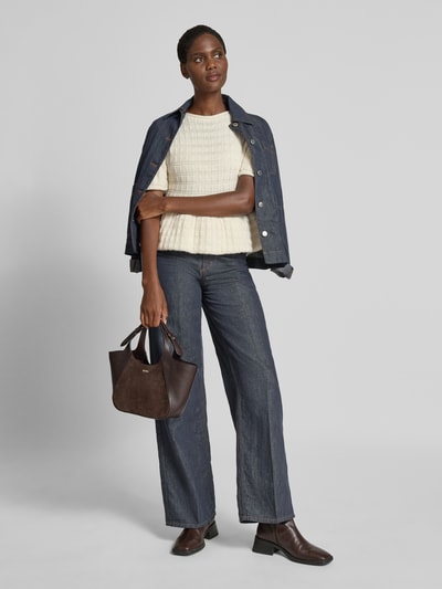 Frauenmodel trägt Regular Fit Strickpullover mit Woll-Anteil Modell 'DOLL' von Mango, cremefarben, Rundhalsausschnitt, 1/2-Arm, grobe Struktur, kombiniert mit blauer Jeansjacke und Jeans, Ganzkörperansicht von vorne.