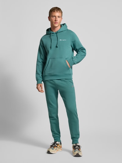 Männermodel trägt Sweatpants mit elastischem Bund und Label-Stitching von CHAMPION aus Baumwoll-Mix, Regular-Fit, Ganzkörperansicht von vorne.